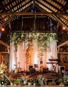 a stage set up for a wedding with greenery and lights on the ceiling, surrounded by potted plants