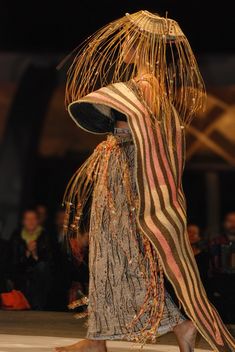 a woman walking down a runway in a dress with fringes on it's head