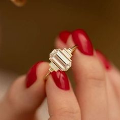 a woman's hand with red nail polish holding a diamond ring