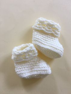 two white crocheted baby booties sitting on top of a table next to each other