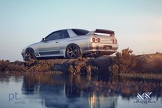 a silver car parked on top of a rock next to a body of water at sunset