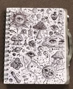 an open notebook with drawings on it sitting on top of a table next to a pen