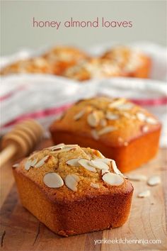 two muffins sitting on top of a wooden cutting board next to a honey almond loaves