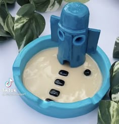 a blue and white water fountain sitting on top of a table next to green leaves