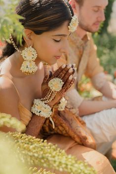 a man and woman sitting next to each other with flowers in their hair on their hands