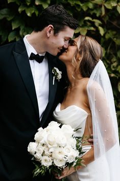 a bride and groom kissing each other in front of greenery on their wedding day