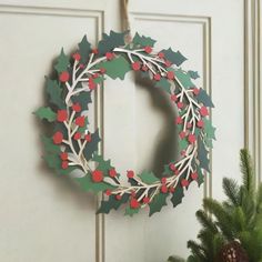 a christmas wreath hanging on the front door with holly and red berry decorations around it