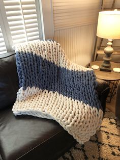 a blue and white knitted blanket sitting on top of a black leather couch next to a lamp