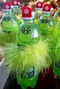 some green water bottles with faces painted on them and furry hair around the tops, sitting in front of a christmas tree