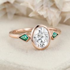 a rose gold ring with an oval cut diamond and emerald accents