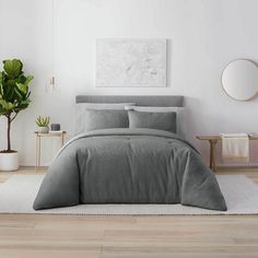 a bedroom with white walls and wood flooring has a gray comforter on the bed