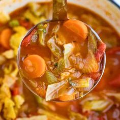 a spoon full of soup with carrots, cabbage and other vegetables in it is being held by a ladle