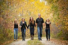 a family walking down a dirt road in the fall with leaves on the ground and trees all around them