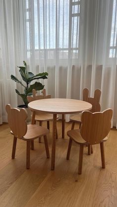 a wooden table with four chairs and a potted plant in front of the window