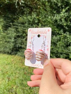 a person holding up a pair of earrings in front of some grass and trees with the words handmade on it