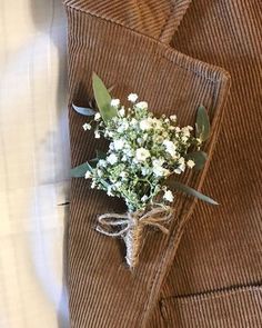 a boutonniere with white flowers is tied to a brown corded jacket