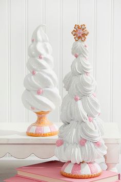 two white christmas trees sitting on top of pink and white books next to each other