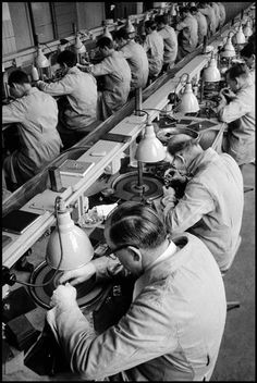 an assembly line with men working on lamps in the factory, one man is using a machine