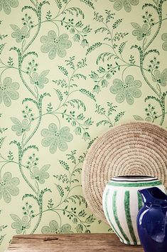 a blue vase sitting on top of a wooden table next to a wallpaper covered in green leaves