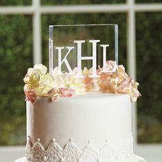 a wedding cake decorated with flowers and the letter kh on top is shown in front of a window