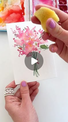 a person holding a piece of paper with flowers on it and a sponge in their hand