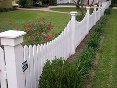 a white picket fence in front of a house with pink flowers on the bushes next to it