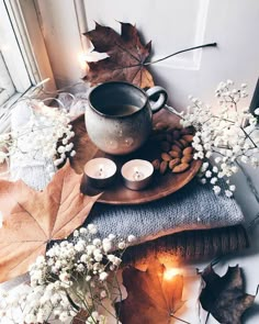 candles, flowers and leaves on a table with a tea light holder in the middle