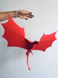 a hand holding a red origami bat hanging from strings