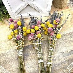 three vases filled with yellow and pink flowers on top of a wooden table next to an envelope