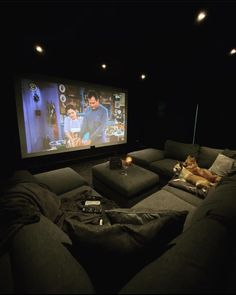 a dog is laying on the couch in front of a large screen with two people watching