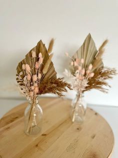 two vases with dried flowers in them on a table