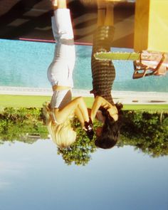 two women are upside down on the ground in front of a pool and trees with their hands up