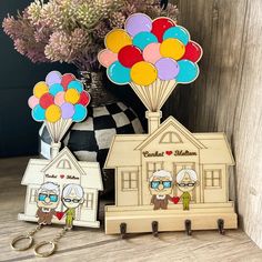 two wooden keychains with balloons attached to them on a table next to a vase filled with flowers