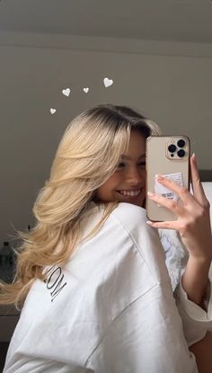 a woman holding up a cell phone in front of her face while wearing a white shirt