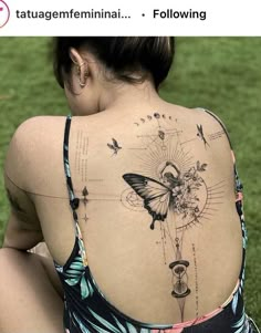 a woman with a butterfly tattoo on her back is sitting in the grass and looking down