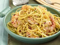 a blue bowl filled with pasta and shrimp on top of a table next to silverware