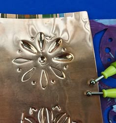 a metal cutting board sitting on top of a blue and purple table cloth with scissors next to it