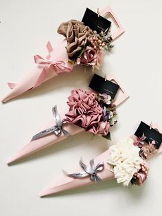 three pink and white flowers are placed in the shape of cones with tags on them