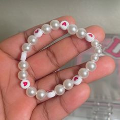 a hand holding a white beaded bracelet with hearts