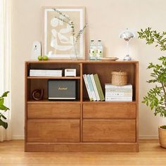 a wooden bookcase with books and plants on top of it in front of a window