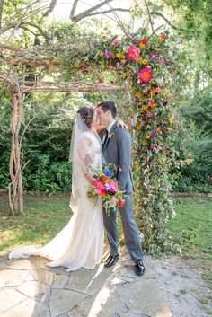 a bride and groom kissing under an arch covered in flowers