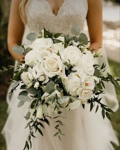 a bridal holding a bouquet of white flowers and greenery in her hands,