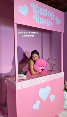 a girl is holding a pink teddy bear in a booth with hearts on the walls