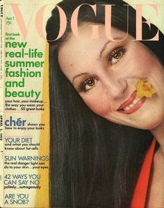 a woman with long black hair on the cover of a magazine that has a yellow flower in her mouth