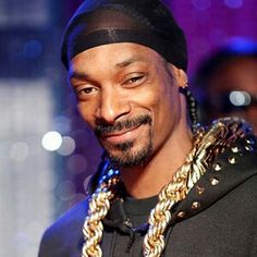 a man in a black hoodie and some gold chains on his neck smiles at the camera