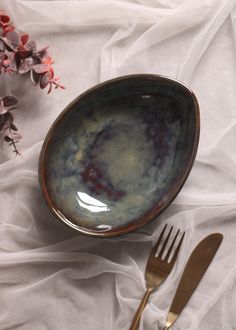 two forks and a bowl on a white table cloth with flowers in the background,