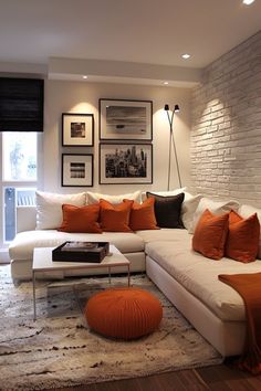 a living room with white couches and orange pillows on top of the rugs