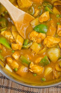 a wooden spoon in a pot filled with vegetables and meats on top of a mat