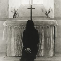 a black and white photo of a woman standing in front of a cross with her hands on her hips