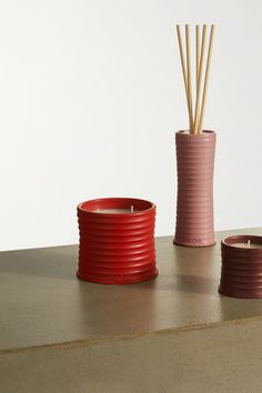 two red cups with reeds in them on a table next to a candle holder